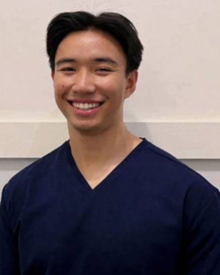 Dr Eddie Suon, Melbourne general dentist, smiling warmly in navy dental scrubs